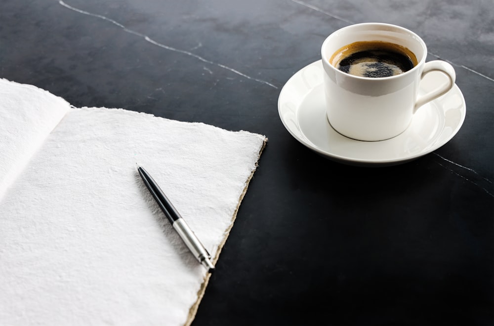 a cup of coffee and a pen on a table
