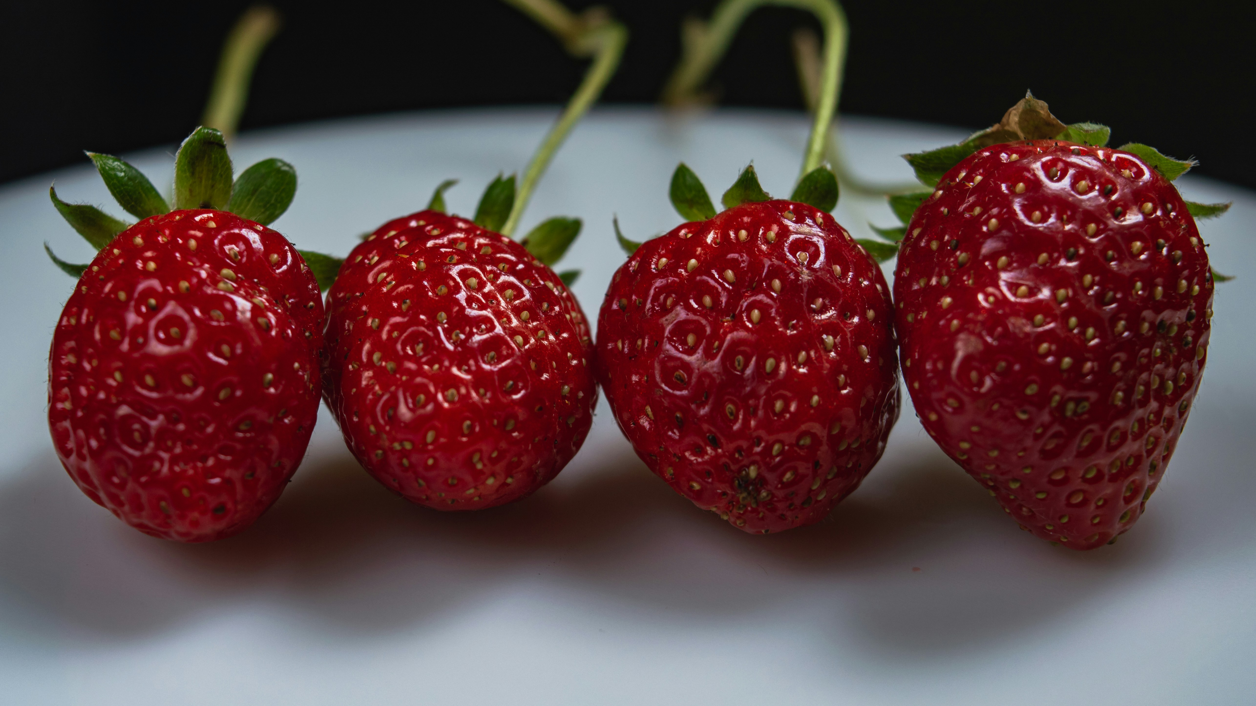 a group of three strawberries sitting on top of a white plate, 
