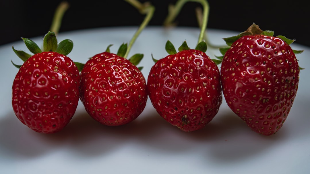 a group of three strawberries sitting on top of a white plate,