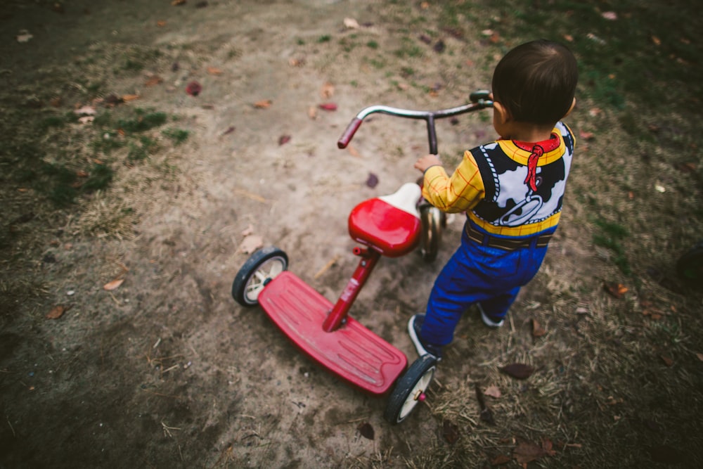 a young boy riding a red tricycle on a dirt road