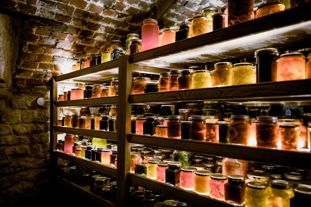 a shelf filled with lots of jars next to a brick wall