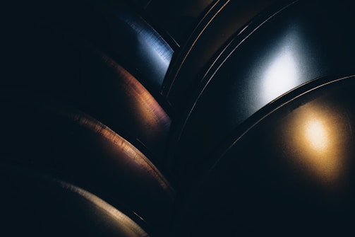 Curved metallic surfaces with a smooth texture reflect light in varying shades, revealing intricate patterns and gradients. The interplay of light and shadow creates a dynamic visual effect.