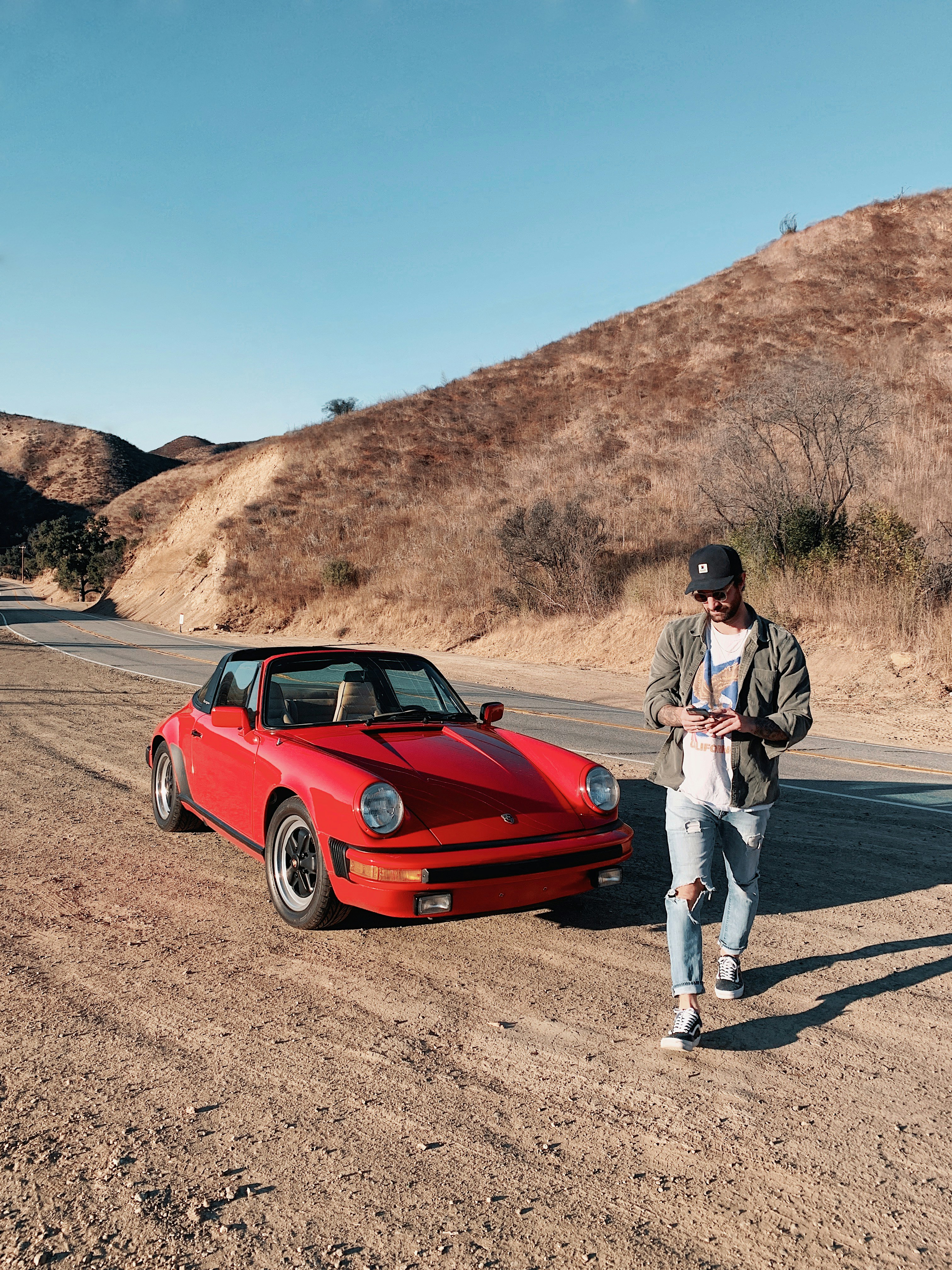 a man standing next to a red car on a dirt road