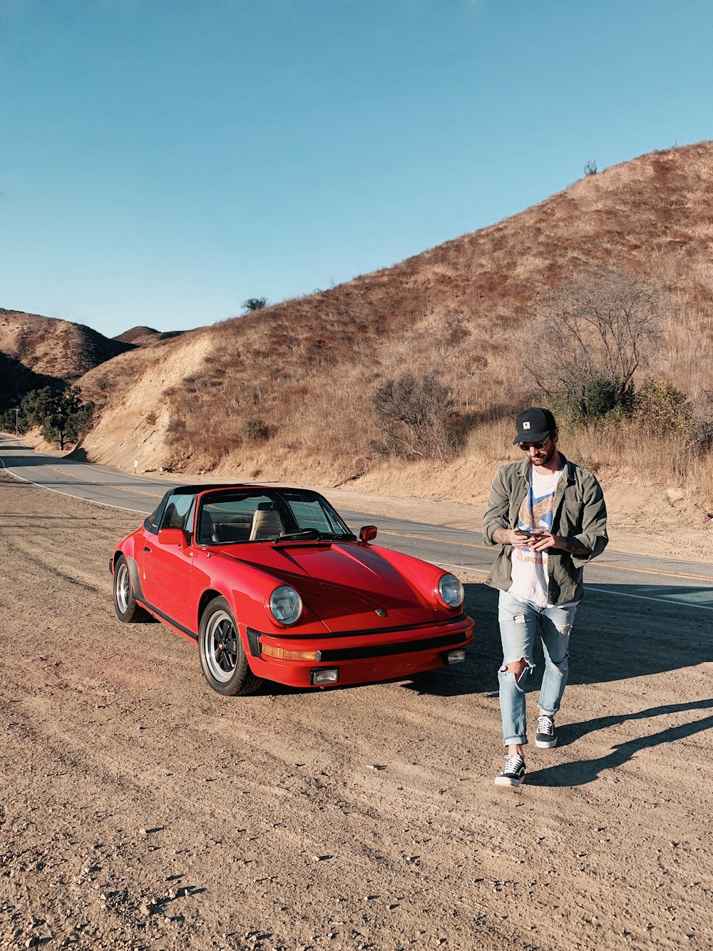 a man standing next to a red car on a dirt road