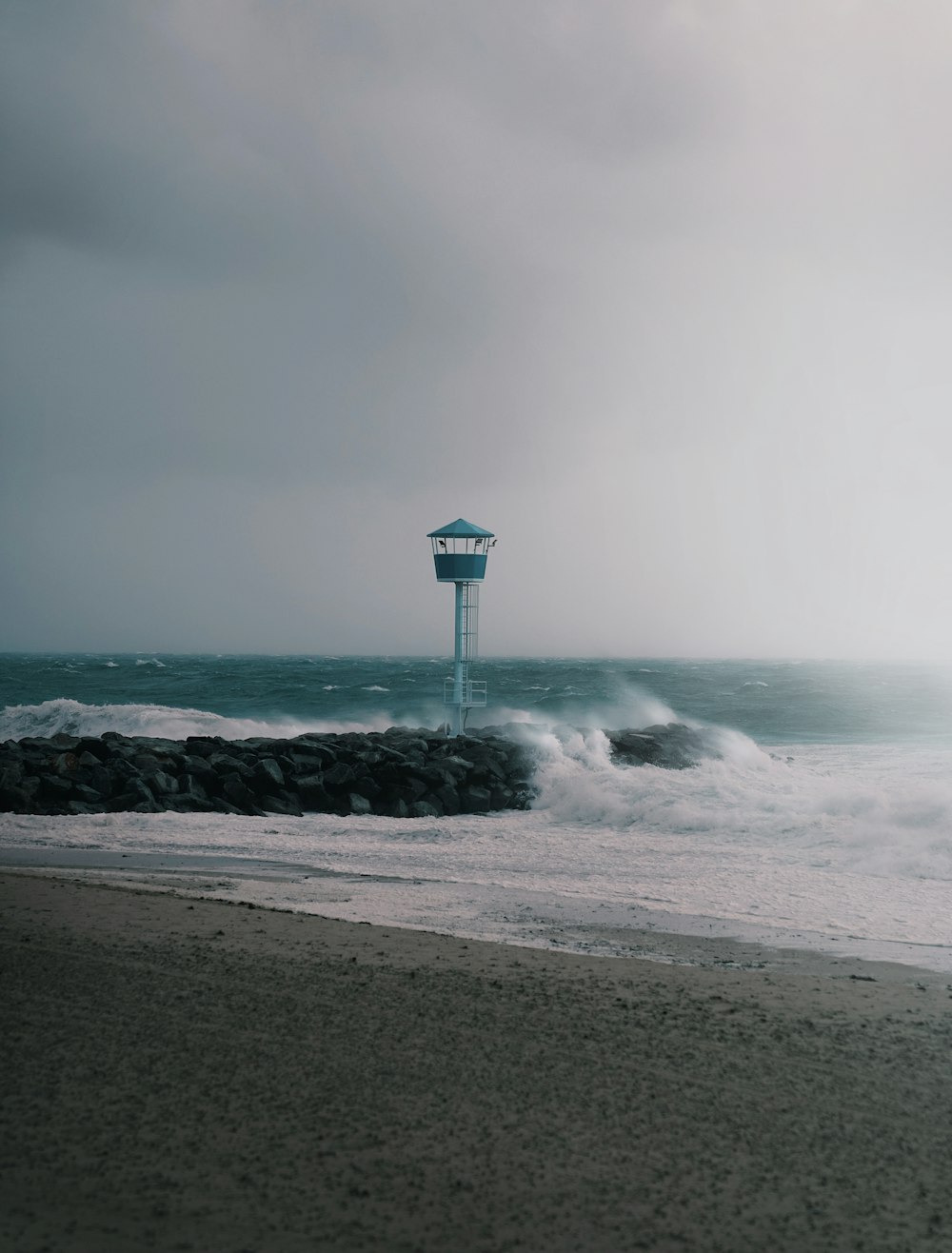 a lighthouse on a beach with waves crashing in front of it