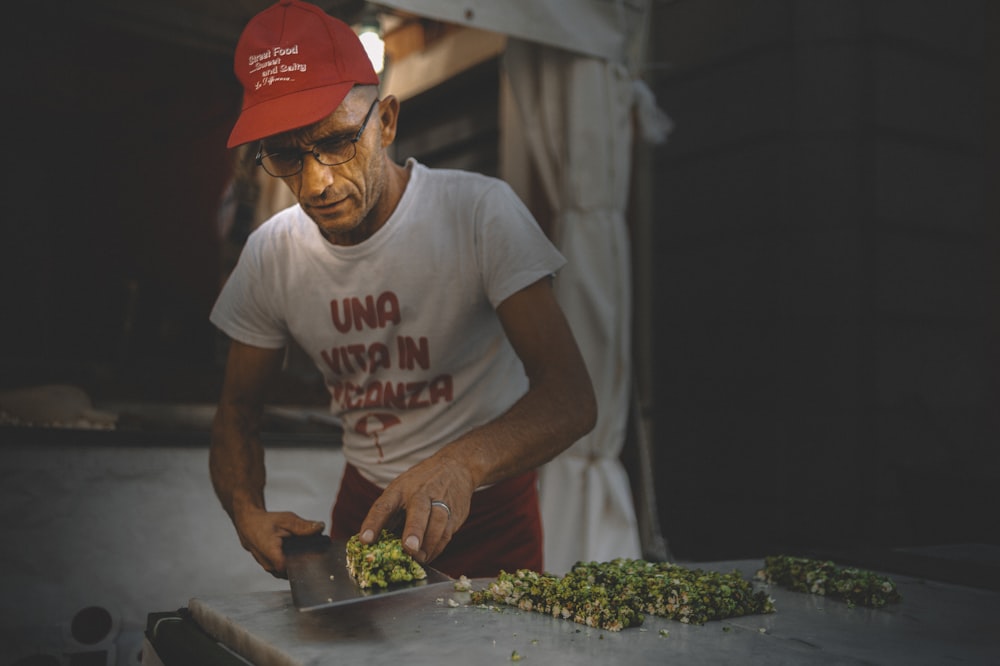 a man in a red hat cutting broccoli on a cutting board