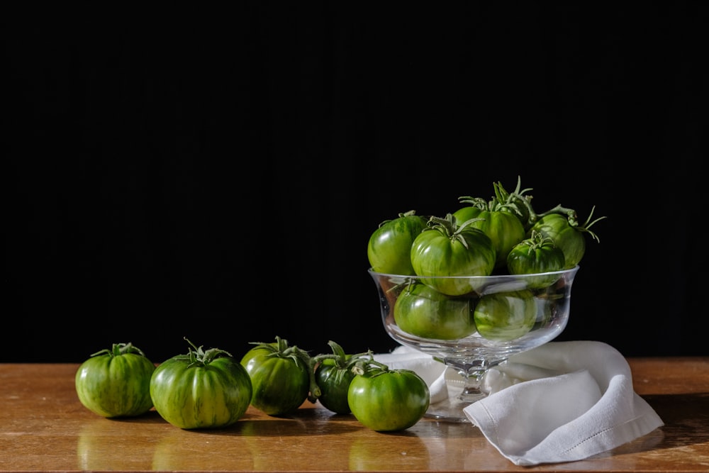 a glass bowl filled with green peppers on top of a wooden table