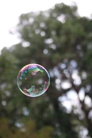 a soap bubble floating in the air with trees in the background
