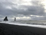 A beach scene showing footprints in dark volcanic sand leading to the crashing waves.
