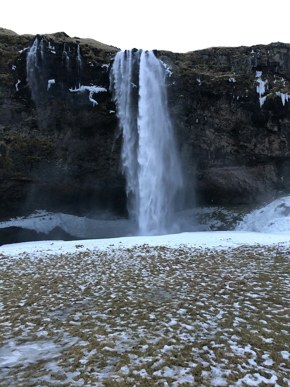 a large waterfall with snow on the ground