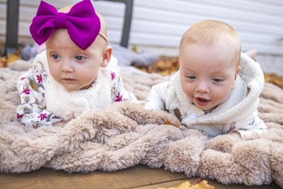 Two twin baby girls playing with colorful toys on a soft rug.