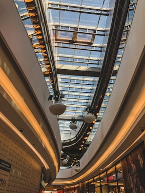 A modern shopping mall exterior bathed in natural light with green landscaping.
