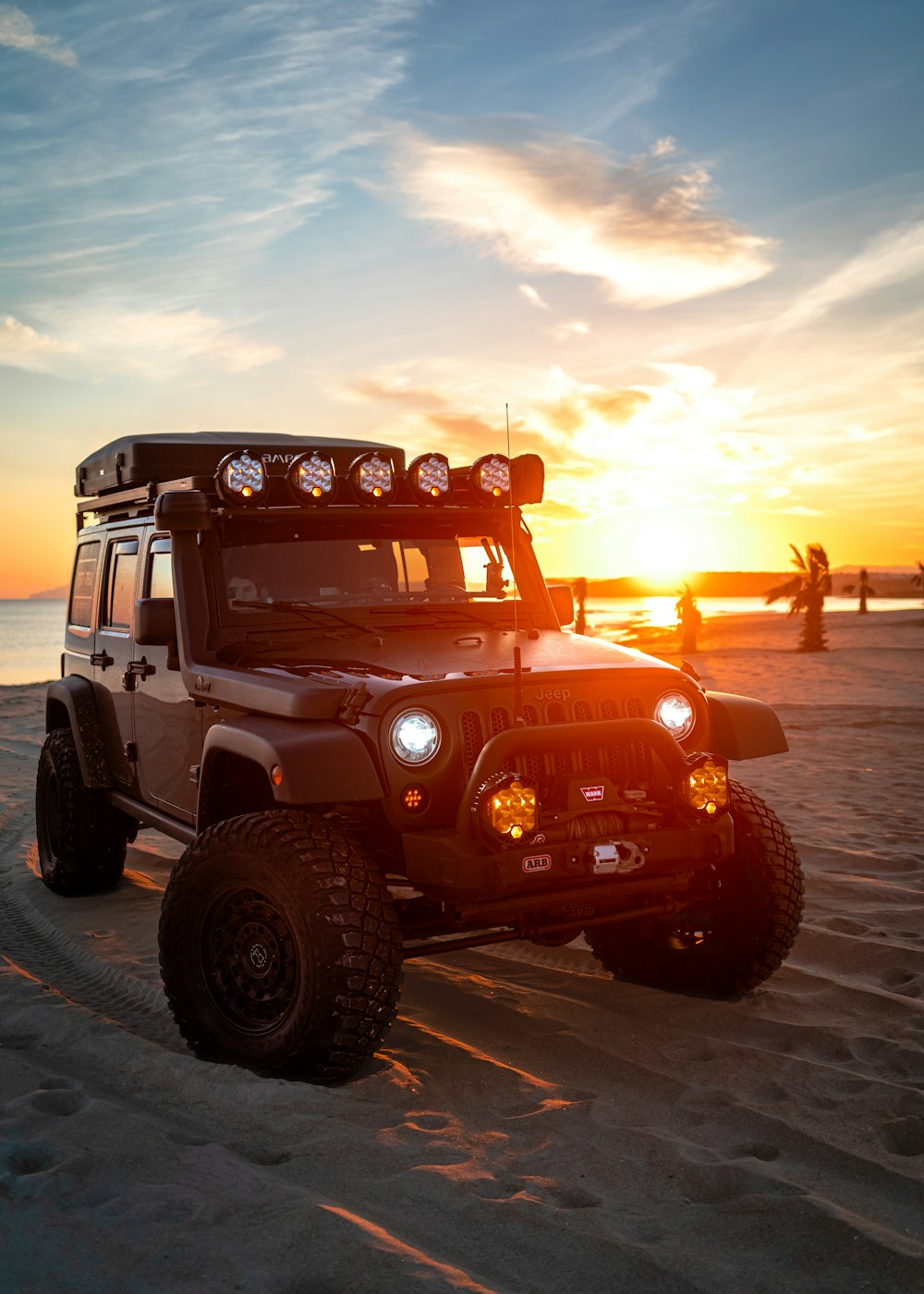 a jeep is parked on the beach at sunset