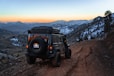 a jeep driving down a dirt road with mountains in the background