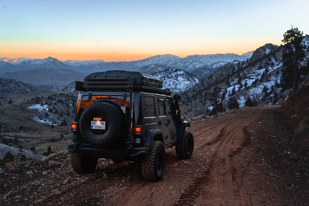 Ein Jeep fährt eine unbefestigte Straße mit Bergen im Hintergrund hinunter