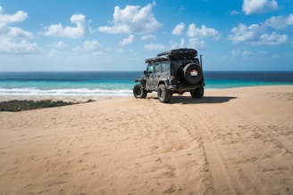 A rugged 4x4 vehicle driving along a sandy beach with turquoise lagoon waters.