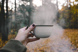 A rugged enamel mug steaming beside a crackling campfire on a foggy riverbank at dawn.