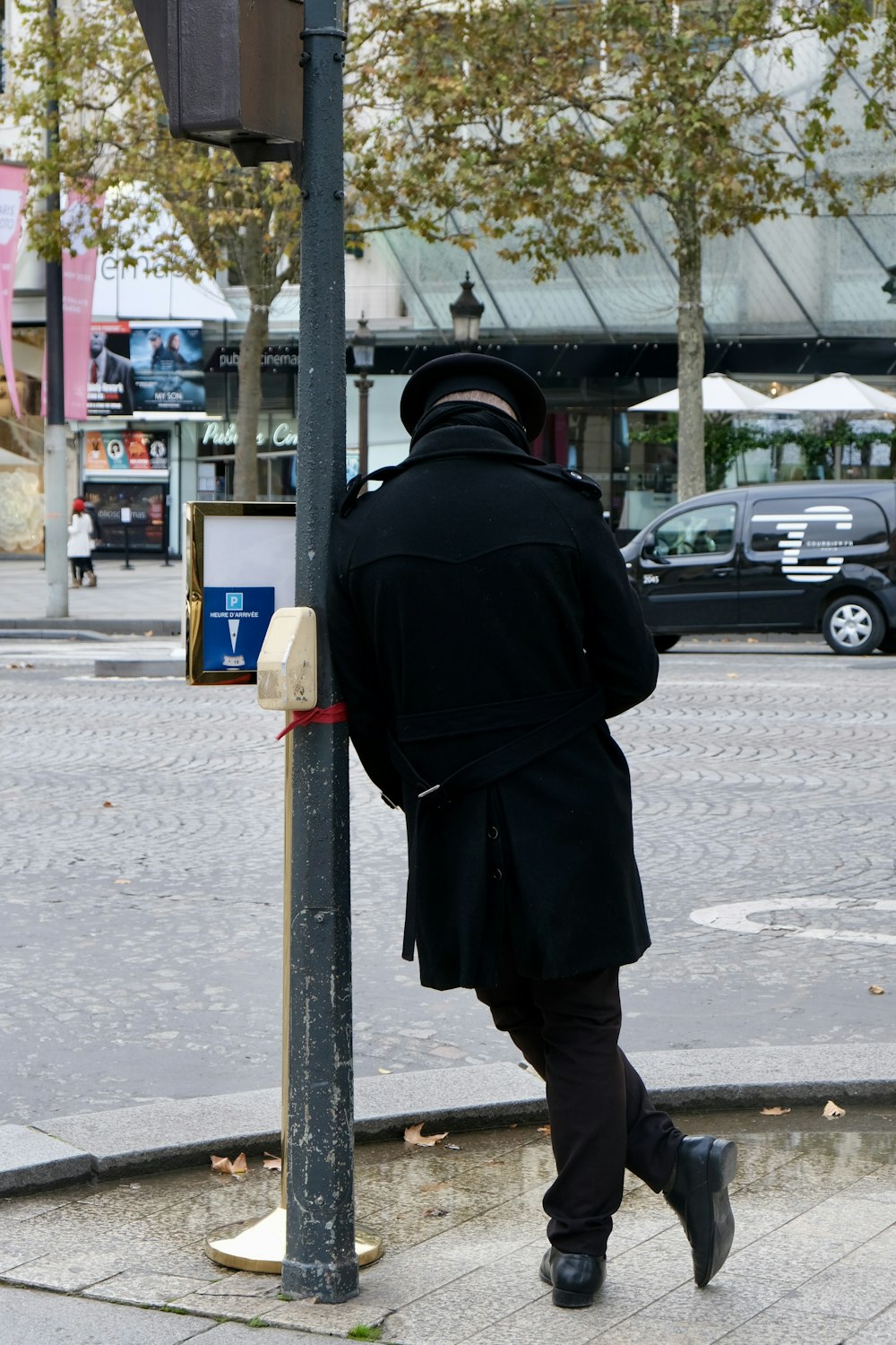 a man in a black coat leaning against a pole