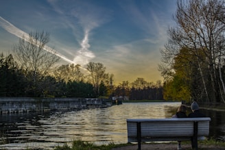 Couple relaxing on a bench overlooking the calm river at golden hour