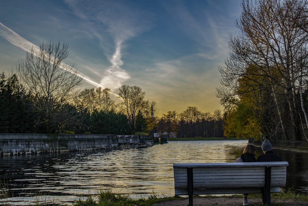 two people sitting on a bench near a body of water