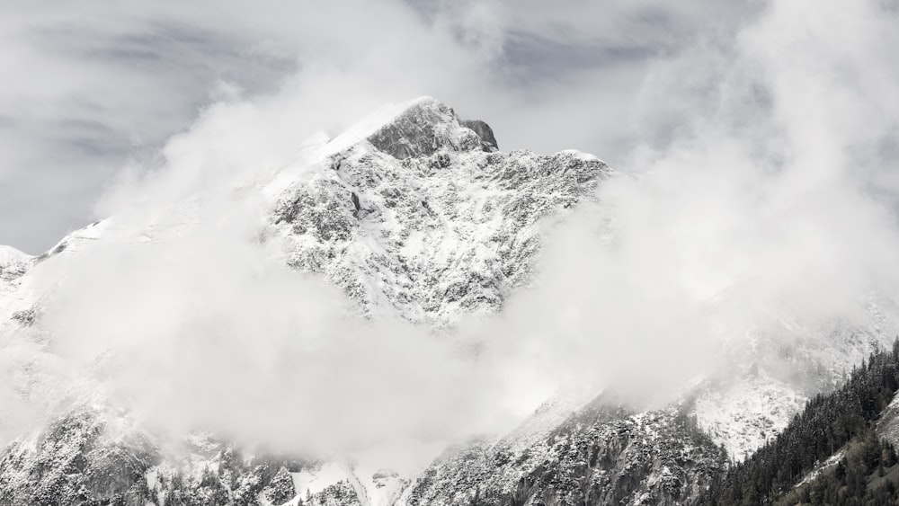 a mountain covered in snow and clouds under a cloudy sky