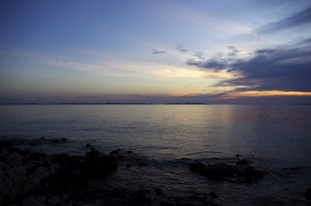 the sun is setting over the ocean on a cloudy day