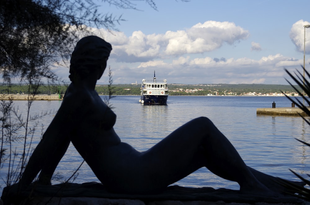 a statue of a person sitting on a rock near a body of water