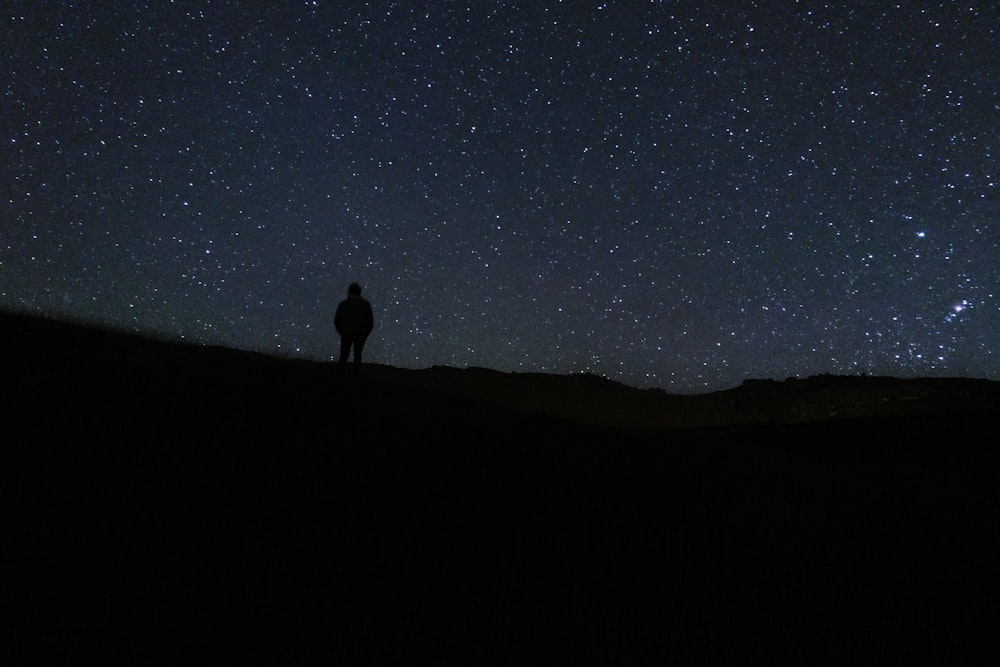 a man standing on top of a hill under a night sky filled with stars