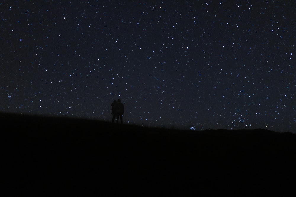 a man standing on top of a hill under a night sky filled with stars