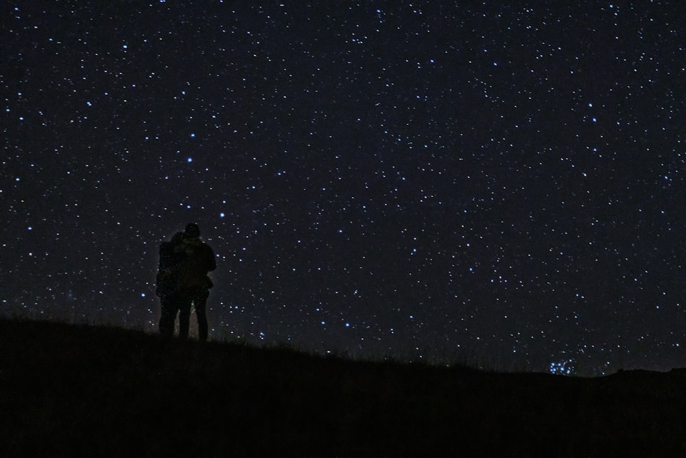a couple of people standing on top of a hill under a sky full of stars