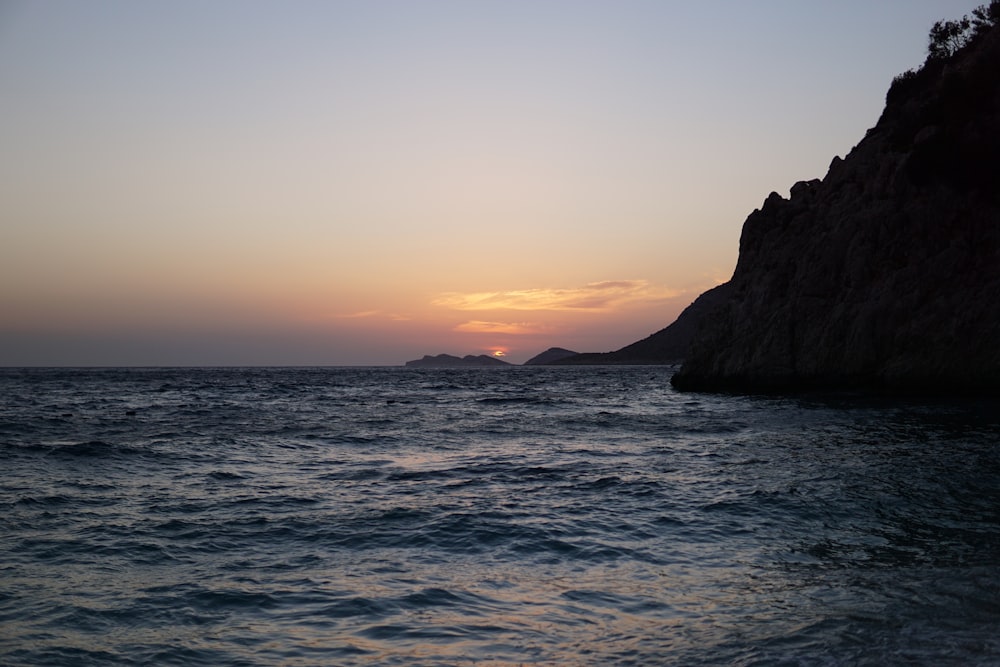 the sun is setting over the ocean with a rock outcropping