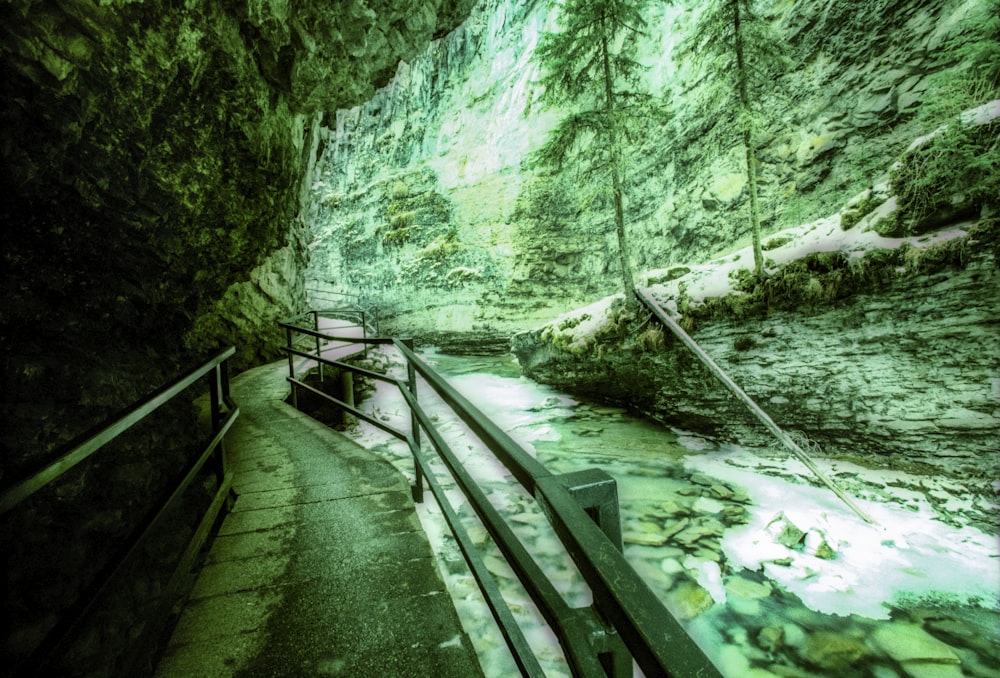 a narrow tunnel with a railing leading to a river