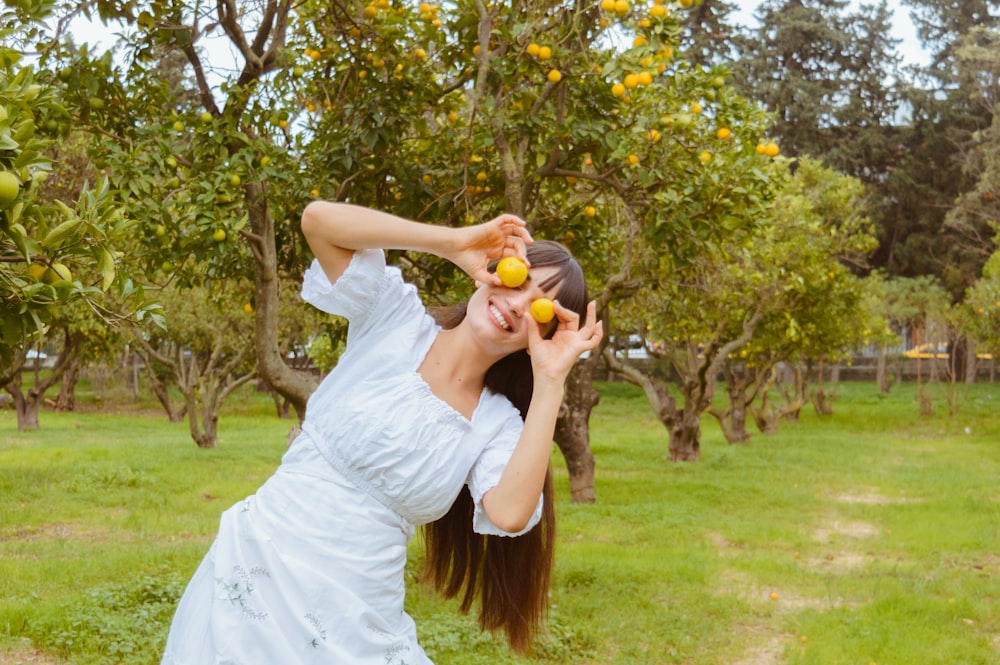 a woman in a white dress holding two oranges