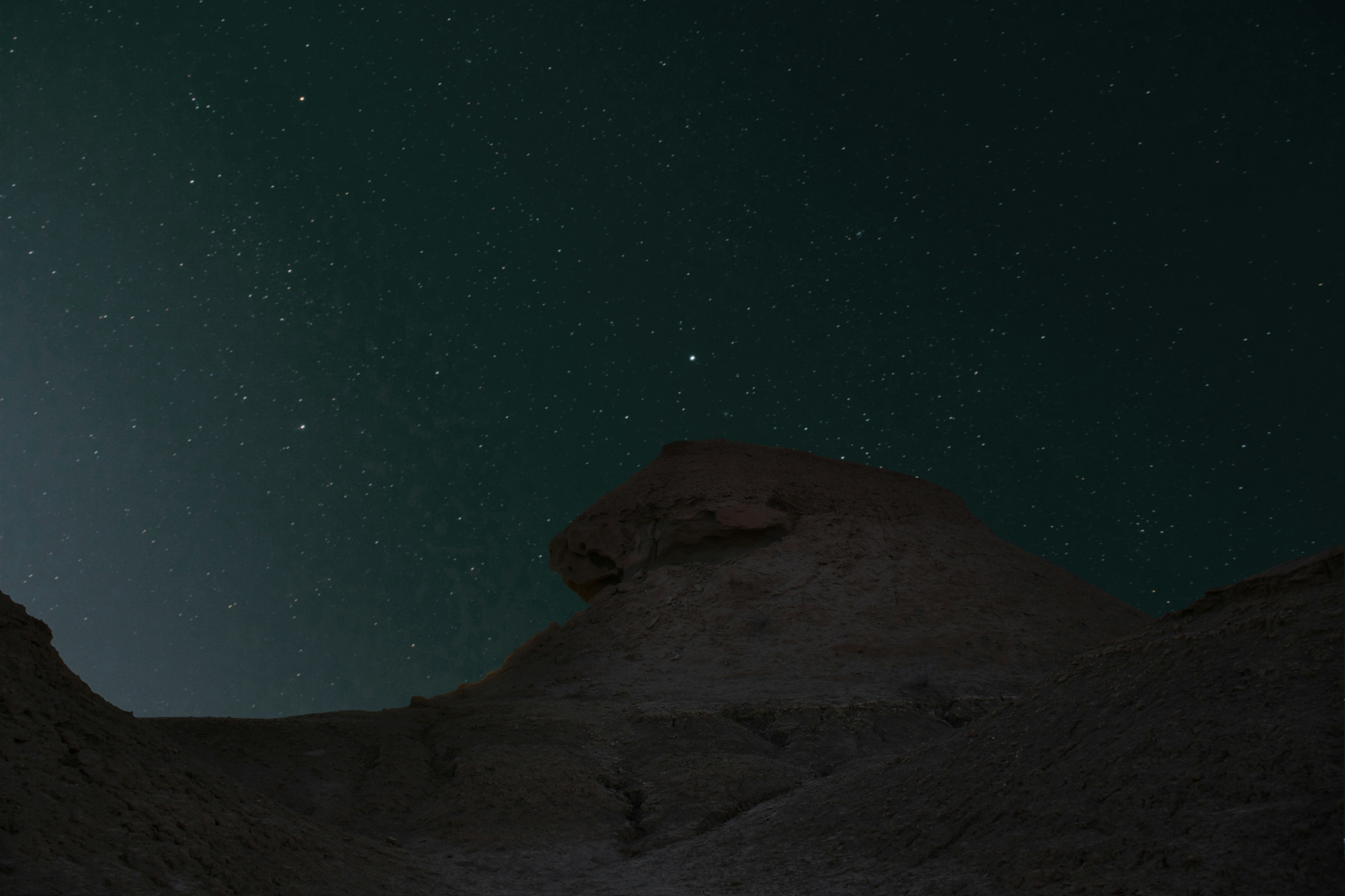 the night sky with stars above a rocky outcropping