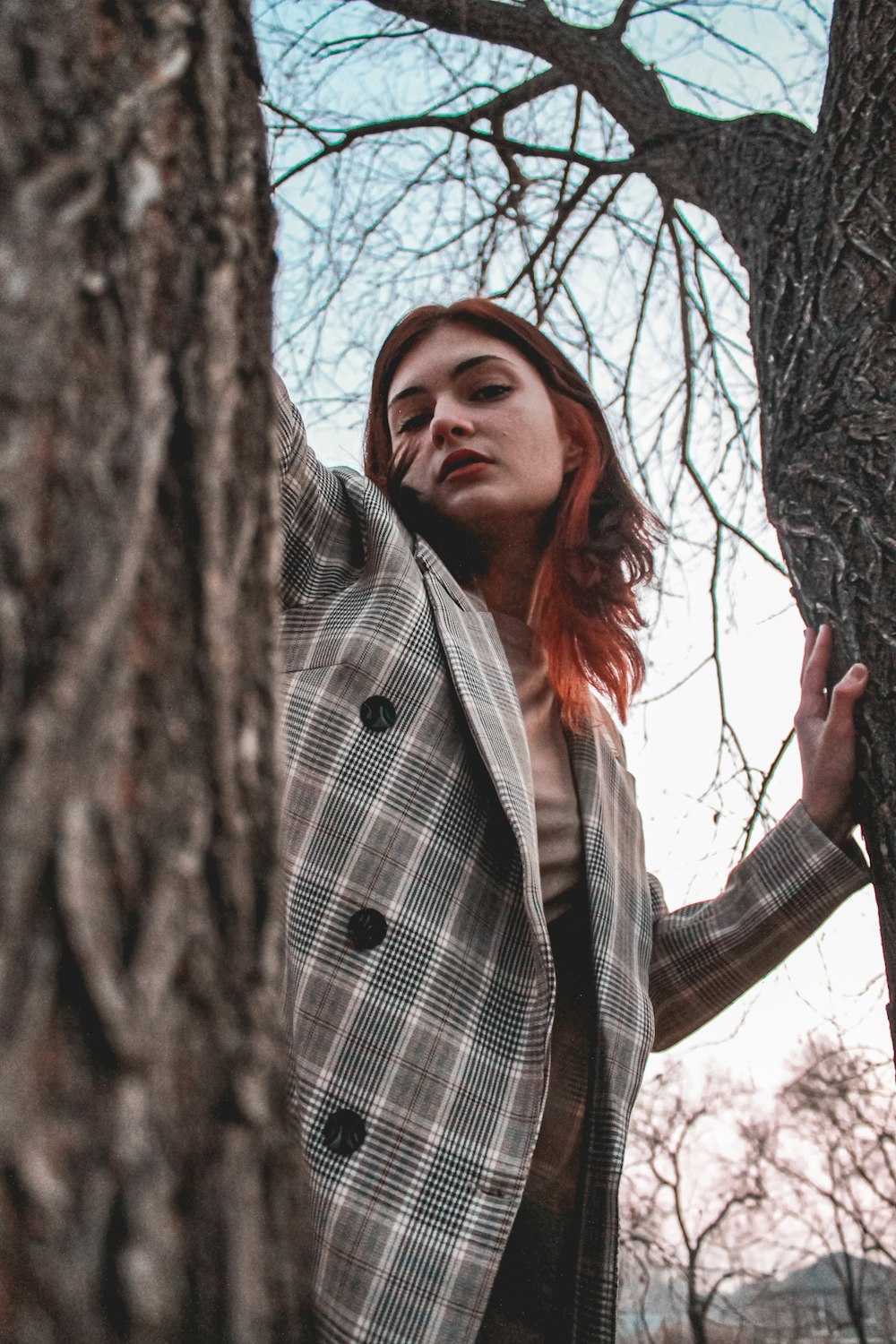 a woman standing next to a tree in a forest