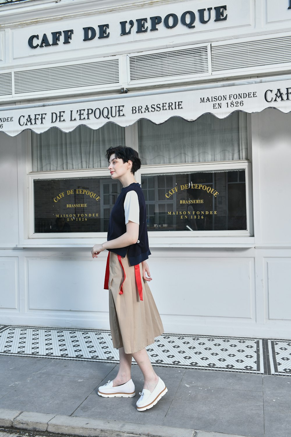 a woman is walking down the sidewalk in front of a cafe