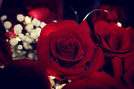 Close-up of deep red flowers and satin fabric details on a wedding table under soft lighting.