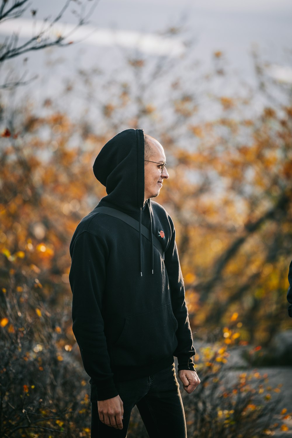 a man in a black hoodie standing in front of a tree