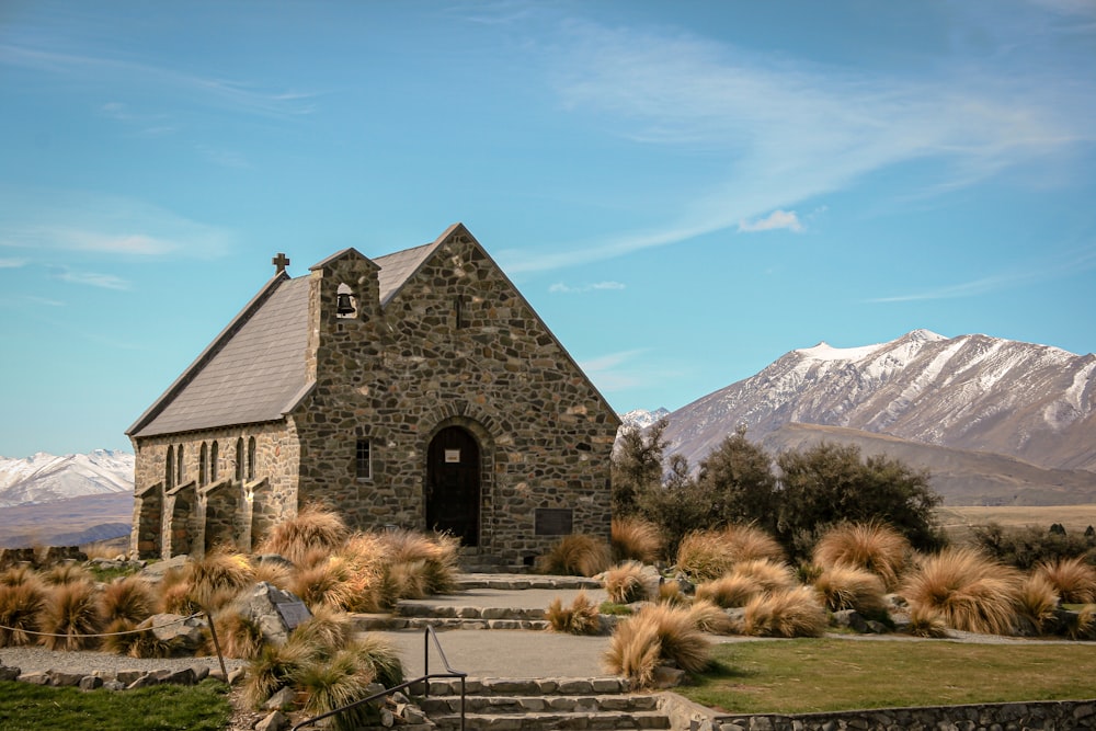 a stone church with a steeple surrounded by grass and mountains