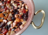 A copper pot filled with a colorful mixture of chopped fruits, including apples, grapes, and berries, creating a vibrant fruit medley. The pot has a detailed brass handle, adding a touch of elegance.