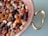 A copper pot filled with a colorful mixture of chopped fruits, including apples, grapes, and berries, creating a vibrant fruit medley. The pot has a detailed brass handle, adding a touch of elegance.