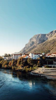 A serene riverside village where travelers engage with local artisans under a bright blue sky.