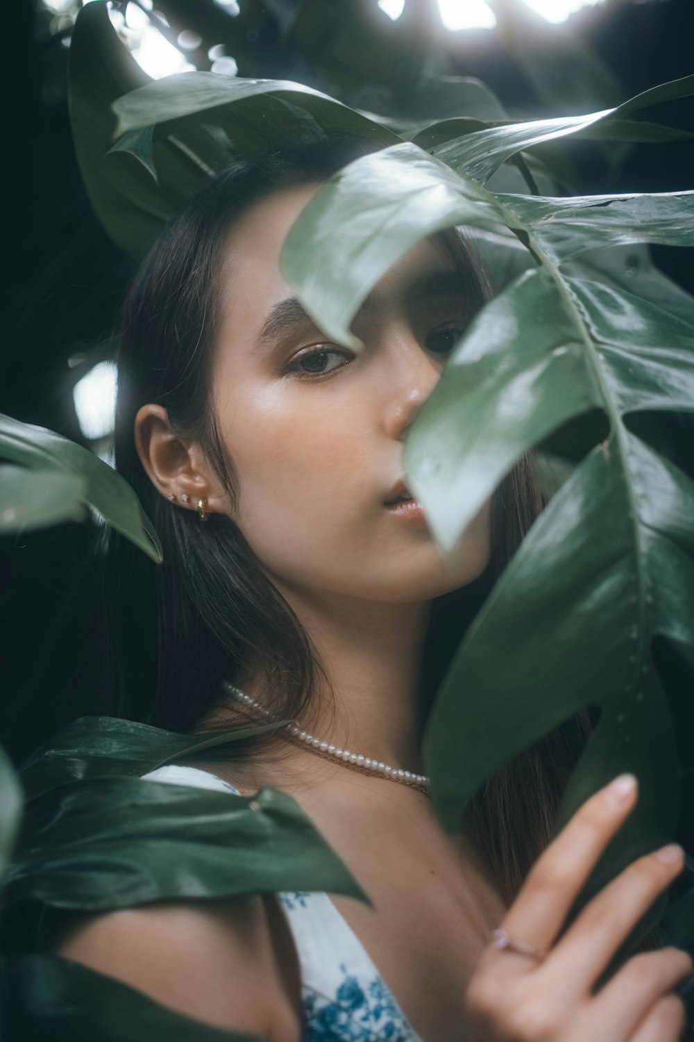 잎이 무성한 녹색 식물 뒤에 서있는 여자