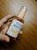 A hand is holding a bottle of YUJA NIACIN Blemish Care Serum, which is labeled with details about its ingredients such as Yuja Extract and Niacinamide. The bottle has a translucent design with a pump dispenser, and it is placed against a wooden background.