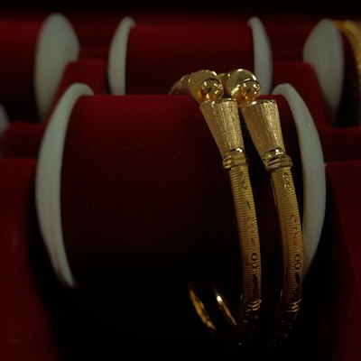 Two intricately designed gold bangles are displayed against a luxurious red velvet background, highlighting the jewelry's elegance and craftsmanship.