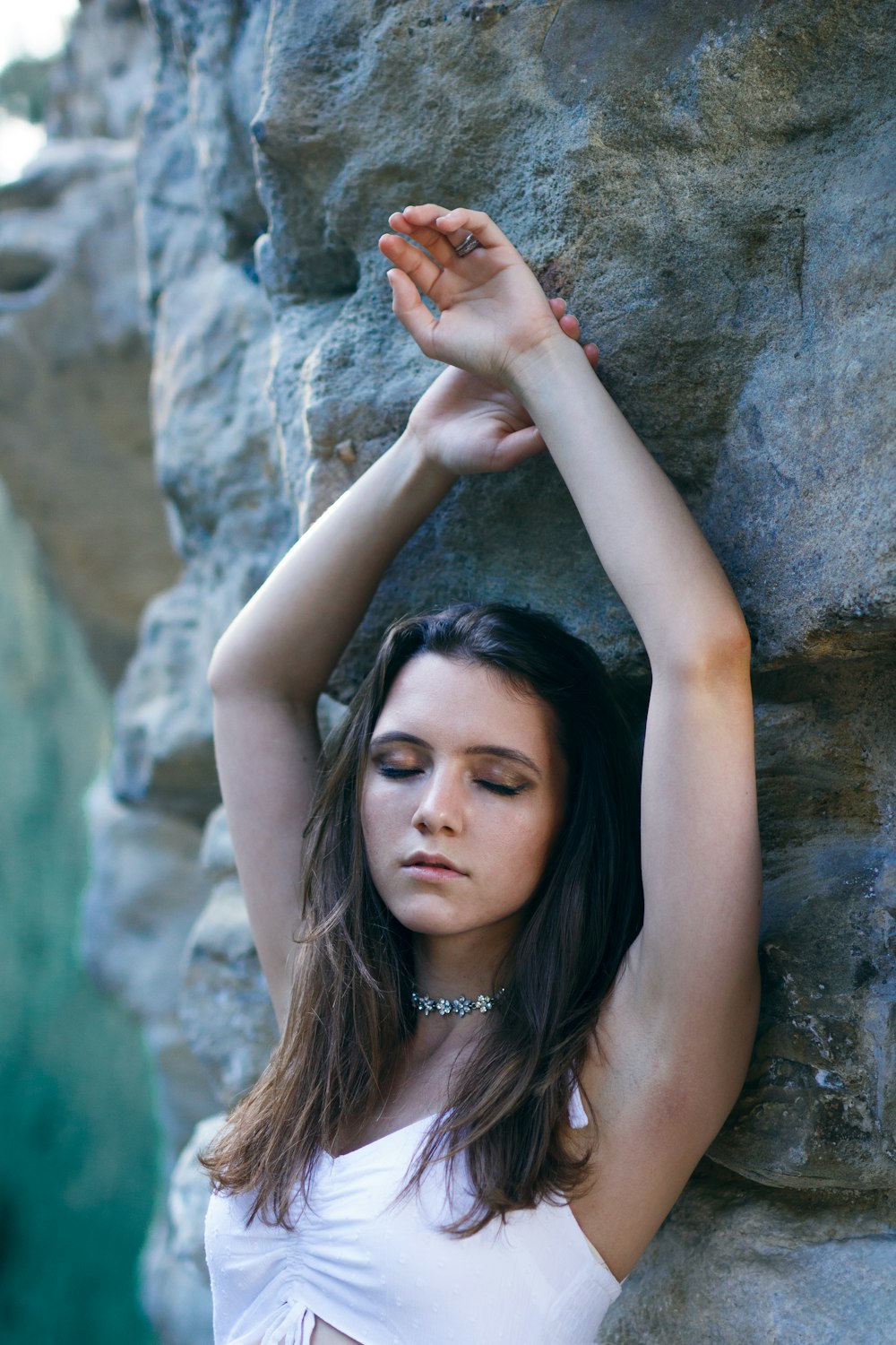 a woman in a white top leaning against a rock