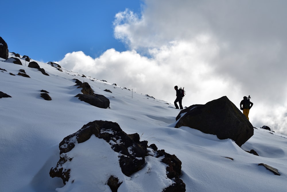 a couple of people climbing up a snow covered mountain