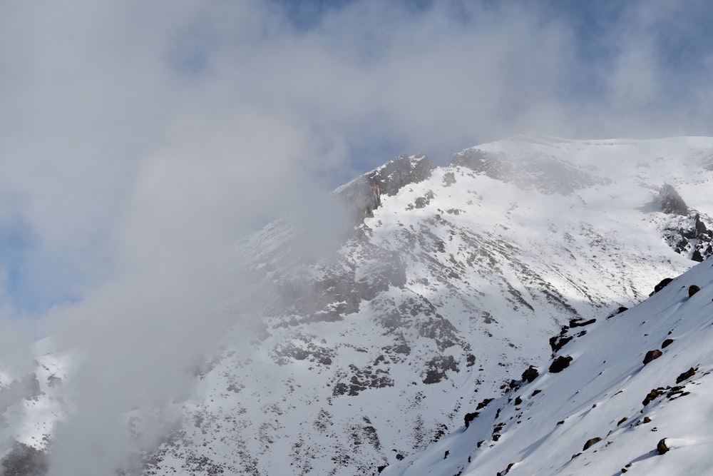 a mountain covered in snow and clouds under a blue sky