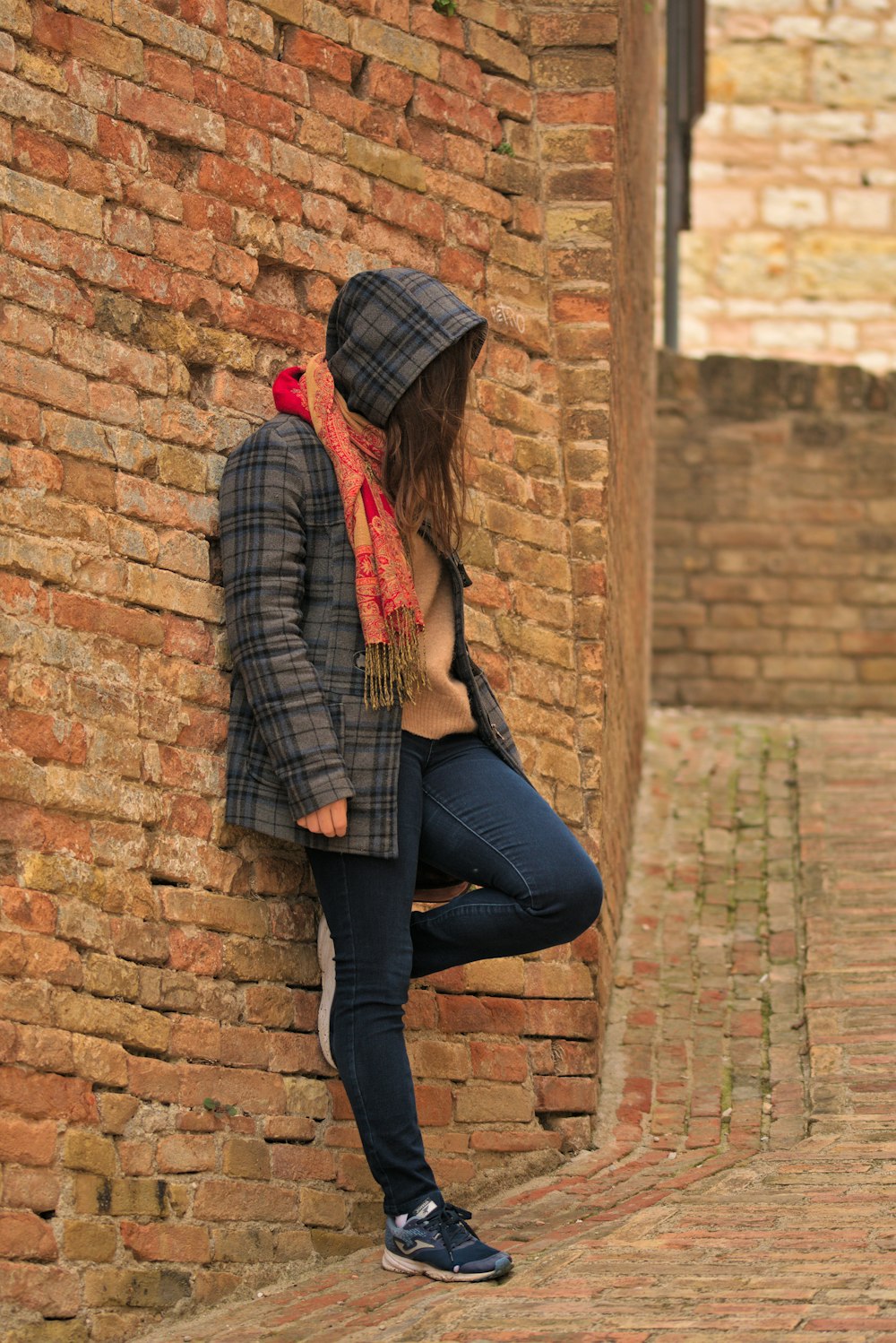 a woman leaning against a brick wall with a scarf around her neck