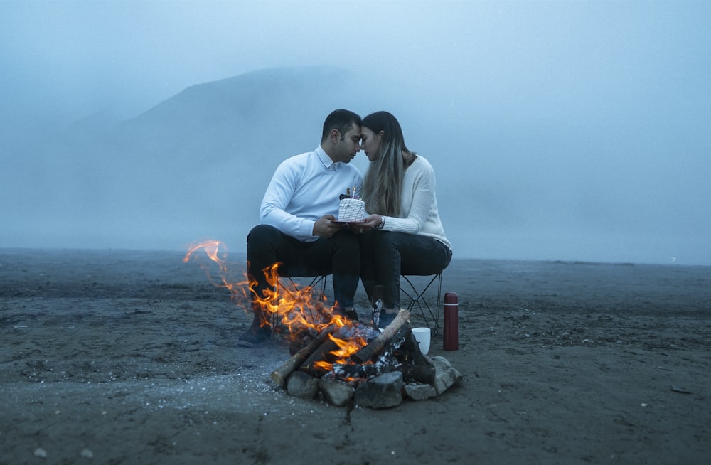 a man and woman sitting next to a campfire